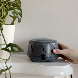 Hand adjusting the power switch on a charcoal Dohm Uno white noise machine beside a potted plant