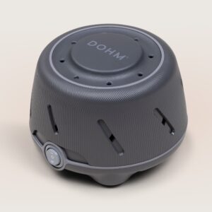 Three-quarter view of Dohm white noise machine showcasing charcoal ribbed housing and front power dial on a neutral beige background