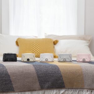 Five Dohm Classic white noise machines in black, cream, white, gray, and pink arranged on a bed with a yellow pillow and striped blanket