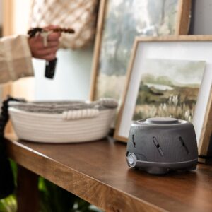 Dohm Elite charcoal white noise machine on a wooden bedside table in a cozy bedroom showing ribbed casing and front control dial