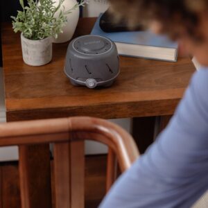 Three-quarter view of Dohm on a wooden bedside table showing charcoal ribbed housing, control dial, and top vents