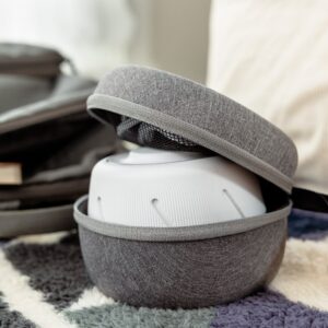 Three-quarter view of Dohm Travel Case open showcasing white Dohm sound machine and padded interior with mesh pocket on a patterned rug