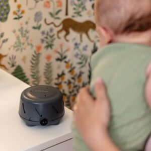 Charcoal Dohm Uno white noise machine on a nursery dresser as a caregiver holds a baby nearby