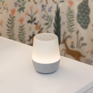 Angled front view of Duet sound machine showing lit night light and top controls with gray fabric base on dresser