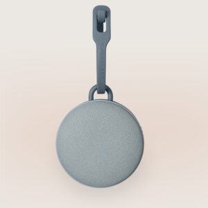 Front view of Hushh 2 travel sound machine showcasing gray fabric speaker grille and silicone hanging strap on pale linen background