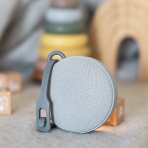 Three-quarter view of Hushh 2 portable sound machine showcasing fabric mesh speaker face and silicone hanging strap in a nursery