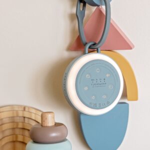 Front of Hushh 2 travel sound machine with illuminated night light ring and hanging clip on pastel nursery background