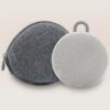 Front of Hushh 2 sound machine with travel case, showcasing compact circular speaker and fabric zip case on pale gradient background