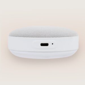Close-up front of Hushh 2 showcasing USB-C charging port and mesh fabric speaker top on a pale beige background