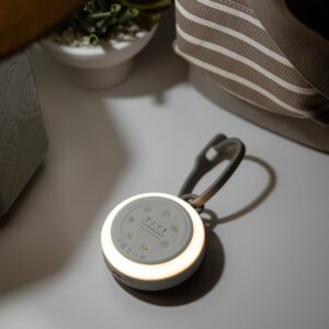 Top-down view of Hushh 2 portable sound machine showing illuminated dimmable night light ring and silicone travel strap on a beige bedside surface