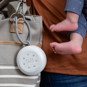Caregiver holding an infant while a white Hushh 2 portable sound machine clips to a striped tote bag