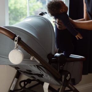 Hushh 2 portable baby sound machine attached to a stroller handle while a parent checks on the child