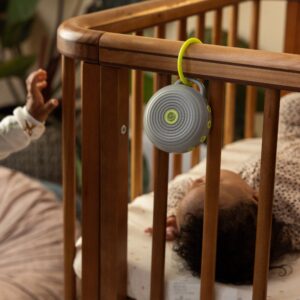 Hushh portable white noise machine clipped to a crib rail in a nursery, soft blanket and stuffed animal nearby