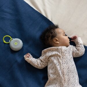 Baby sleeping on a blue blanket beside a Hushh portable sound machine in a cozy nap setting