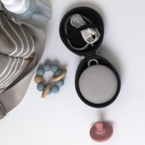Top view of Hushh 2 and travel case showcasing mesh speaker face and USB-C charging cable on a beige background with baby toys