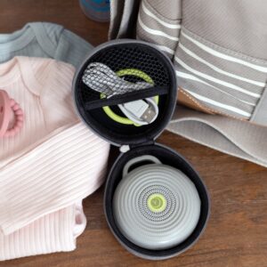Top-down view of Hushh sound machine inside its travel case with charging cable, showing padded linen interior and open zipper on a striped blanket