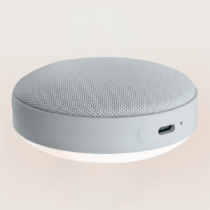 Angled close-up of Hushh 2 portable sound machine showing gray fabric top, USB-C charging port, and glowing night light on a beige background